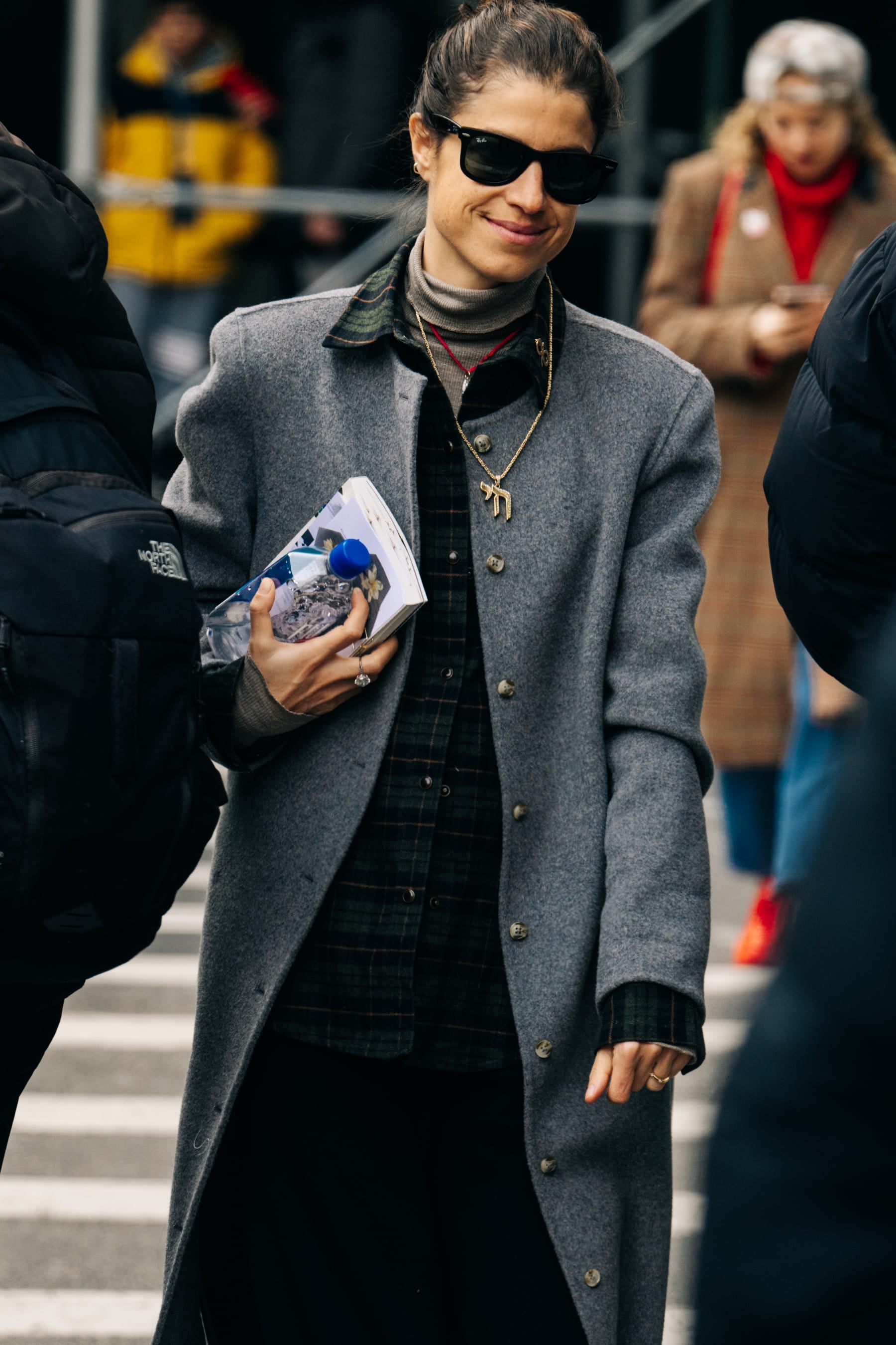 Woman in a gray coat and sunglasses standing on a street