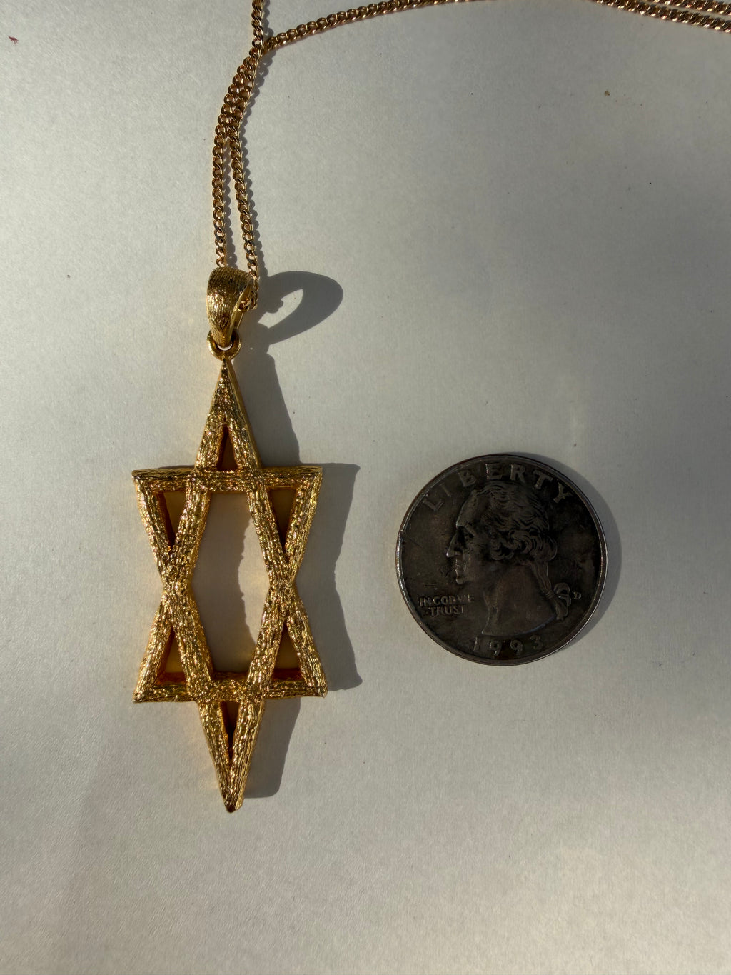 Gold Star of David pendant next to a U.S. quarter for size comparison on a white background