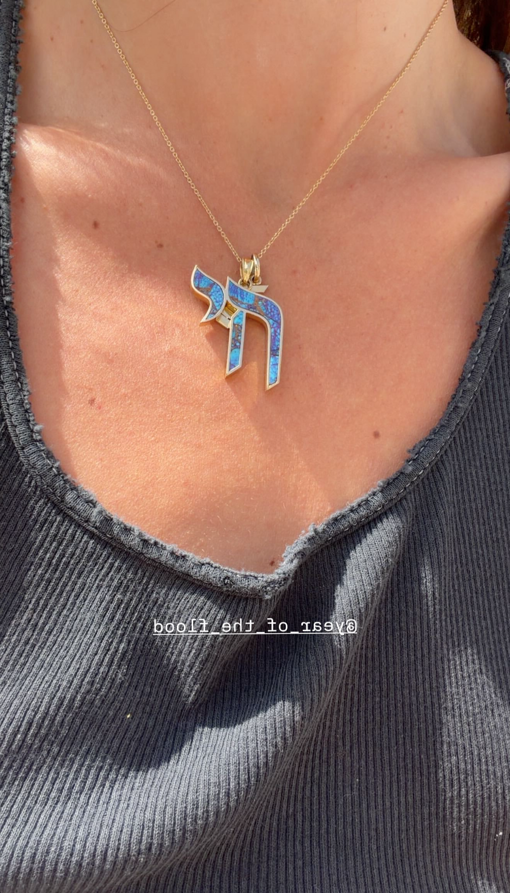 Necklace with a blue pendant worn by a person in a gray sleeveless top.